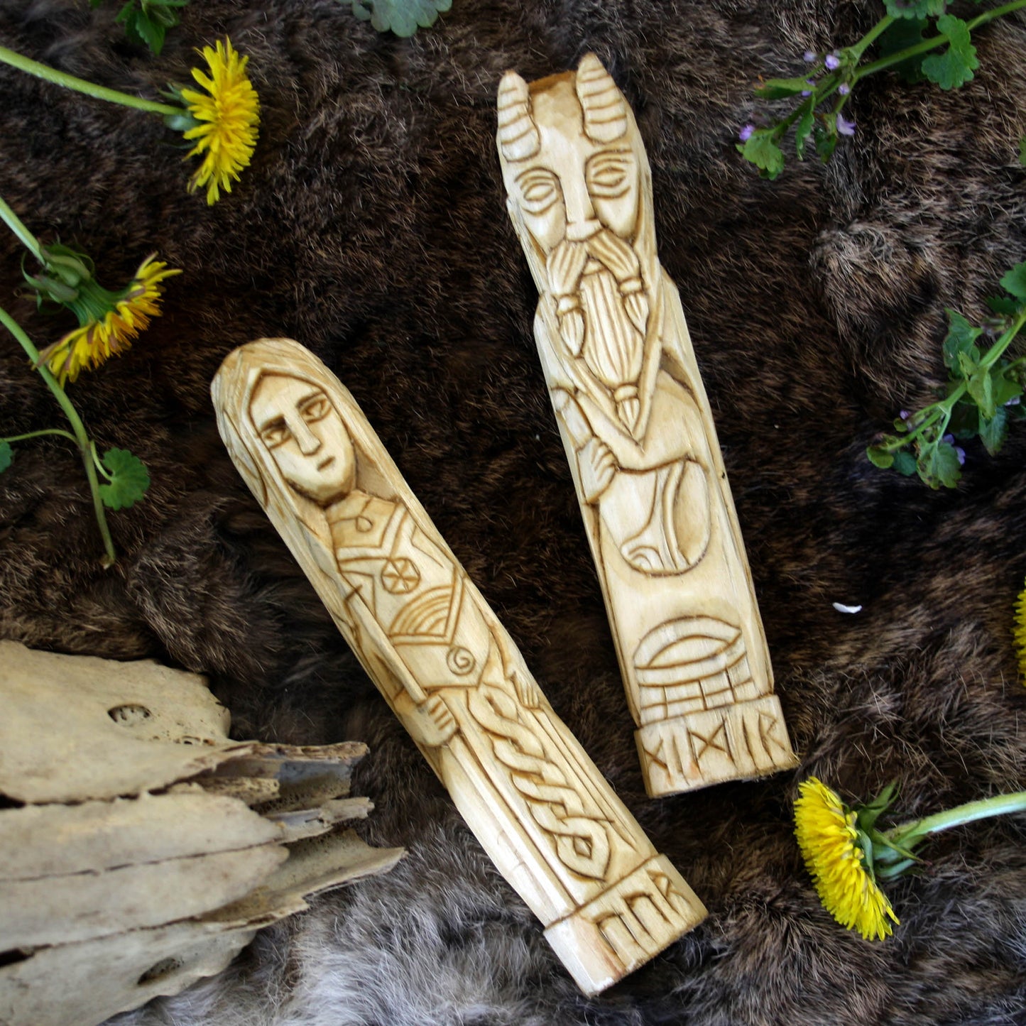 Vor wooden statue with other Norse god hand carved figurines collection on a textured surface with flowers and driftwood.