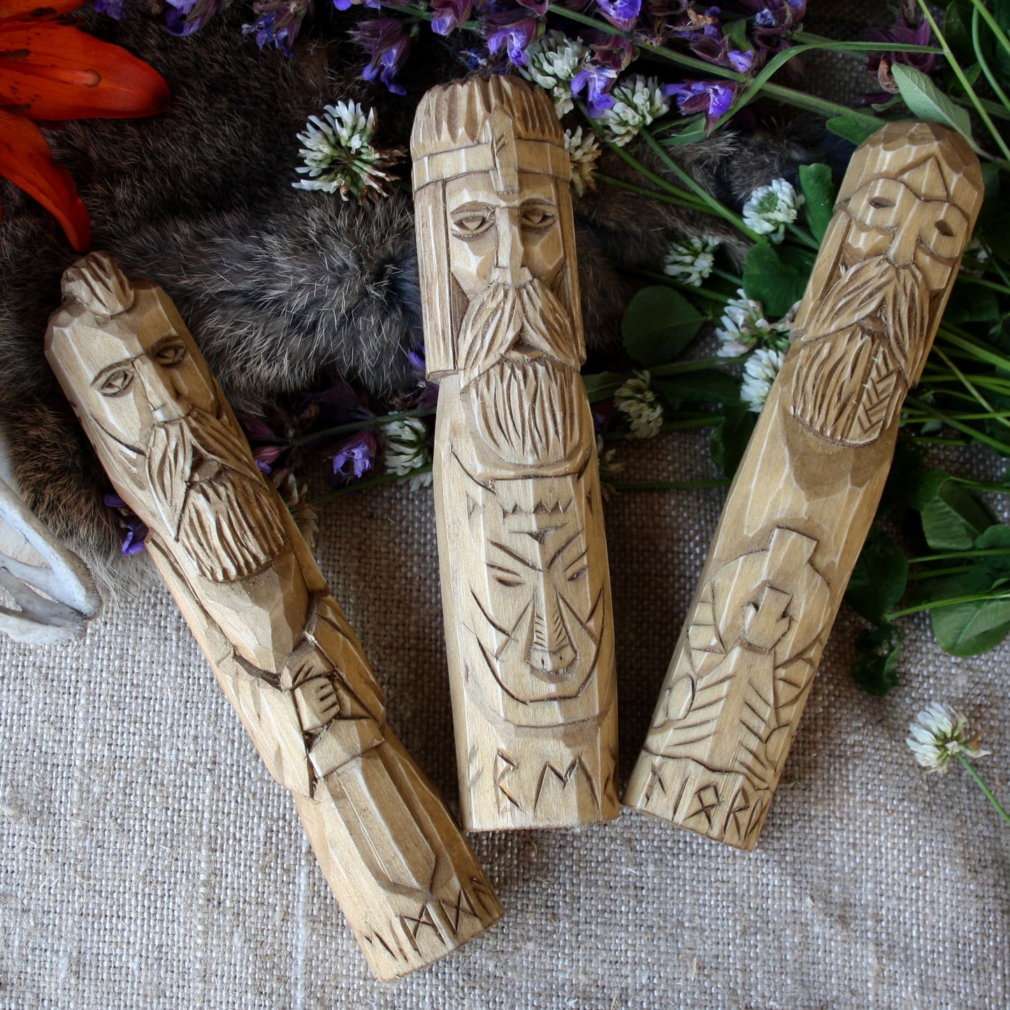 Heimdall wooden statue 18 cm hand carved figurine with other Norse Gods on a textured surface with flowers and leaves.