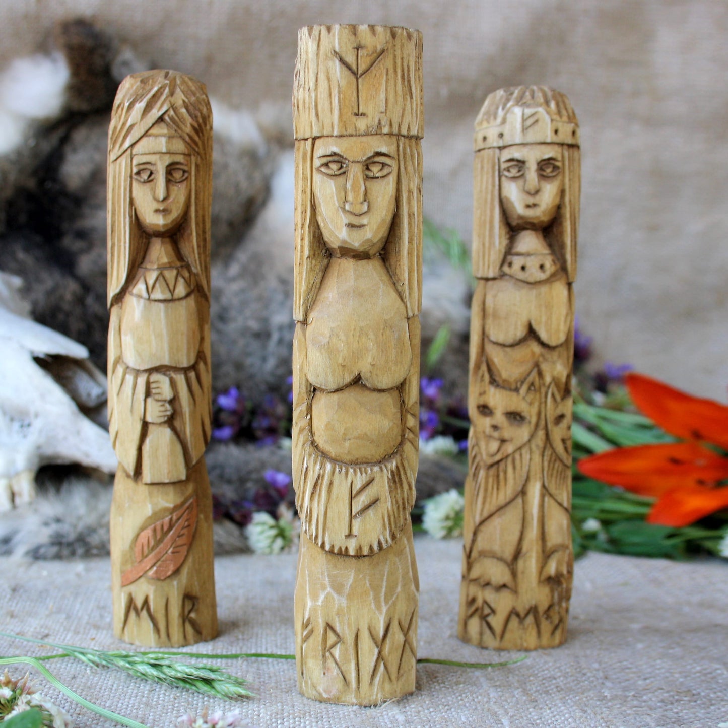 Eir Norse goddess wooden figure with oter Norse goddesses on a textured surface with flowers in the background.