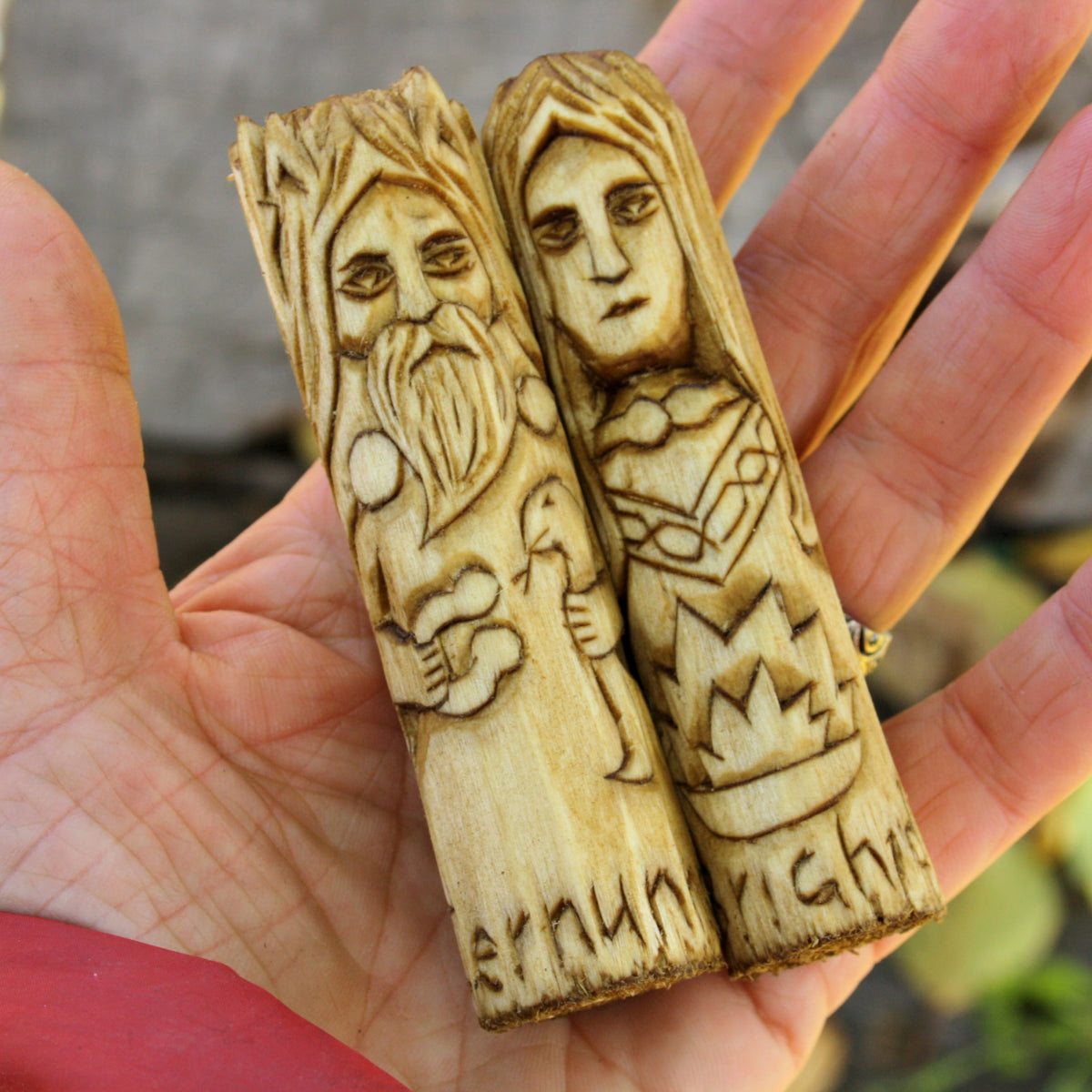 Two 10 cm hand-carved Celtic wooden deity figurines resting on a hand to demonstrate their size