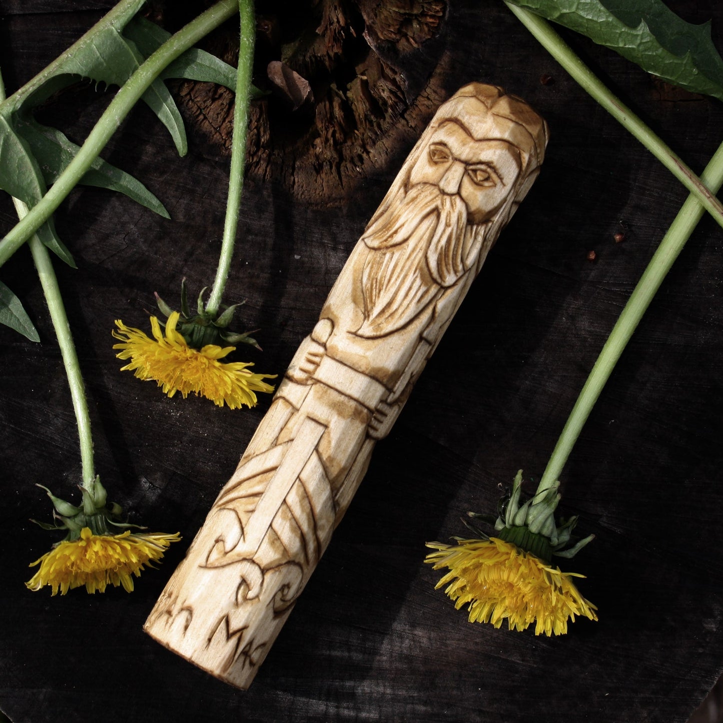 Manannan mac Lir Celtic god of the sea 15cm hand-carved wooden statue styled on a dark wood background with yellow dandelions.