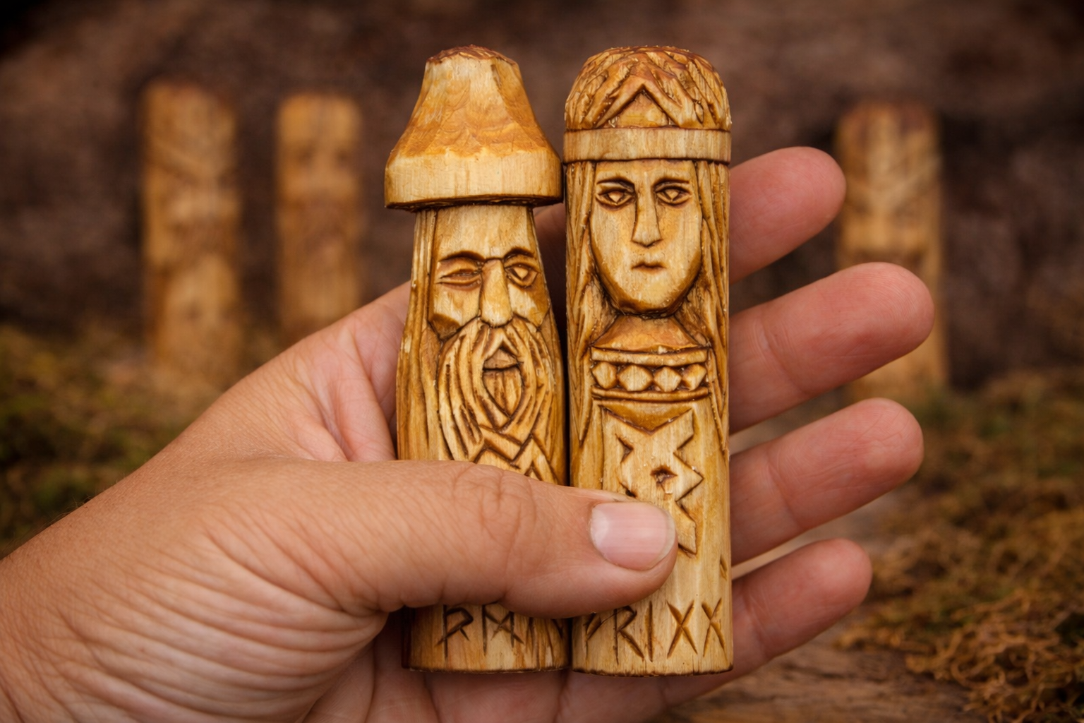 Hand holding two wooden figurines with intricate carvings against a natural background