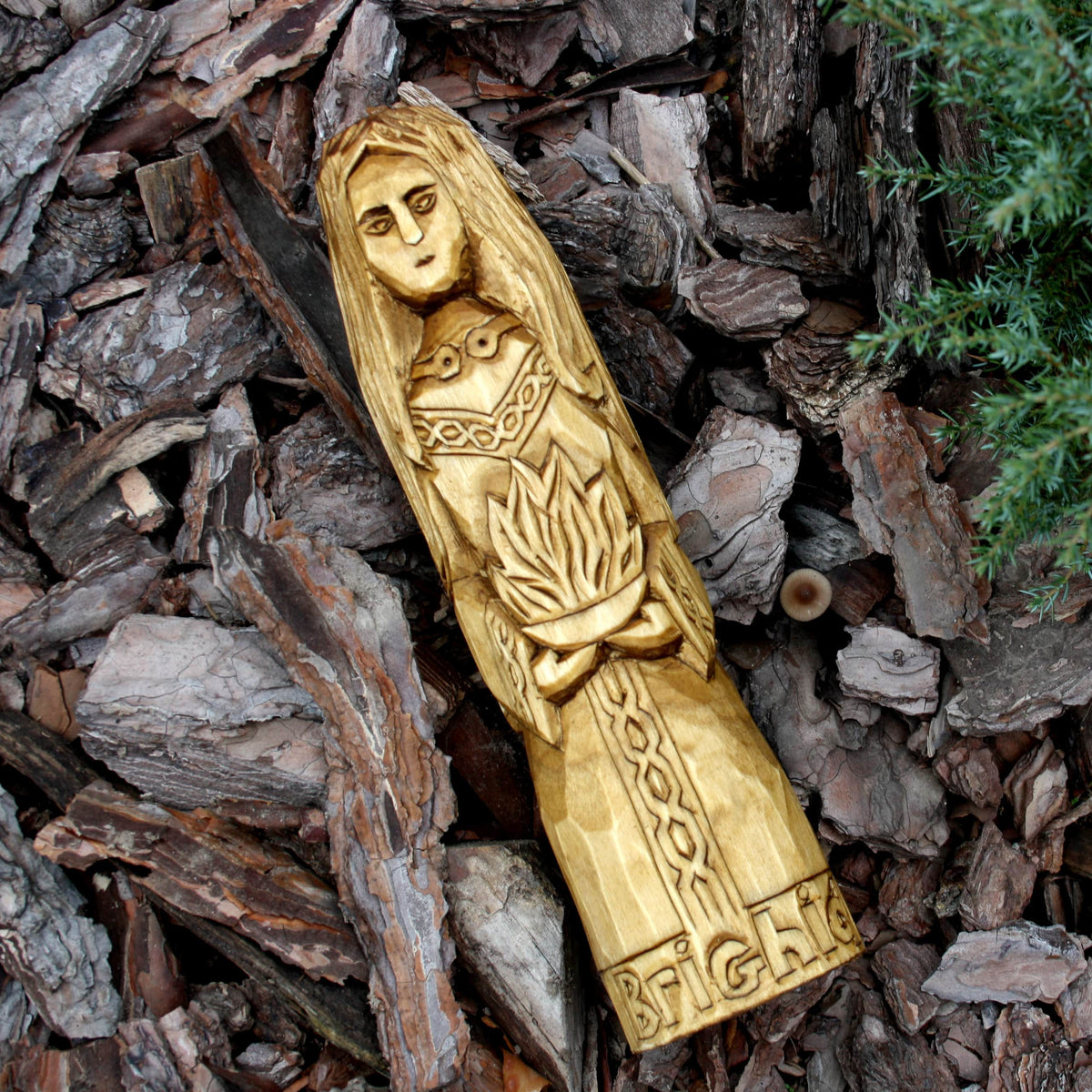 Hand-carved Brigid wooden statue displayed on bark in a natural outdoor setting