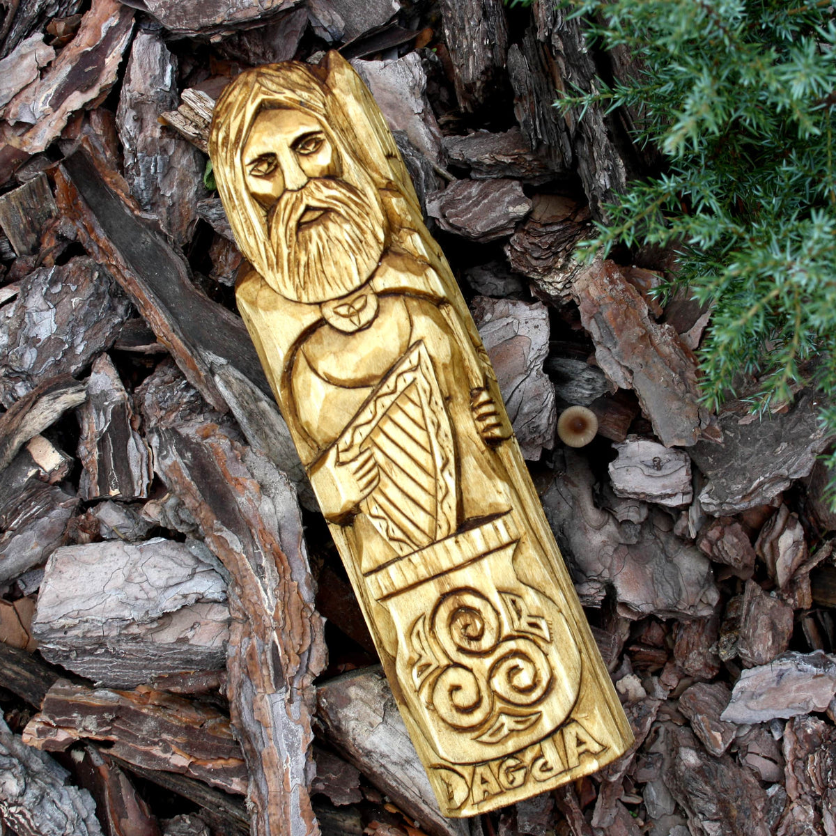 Hand-carved Dagda wooden sculpture displayed on bark in a natural outdoor setting