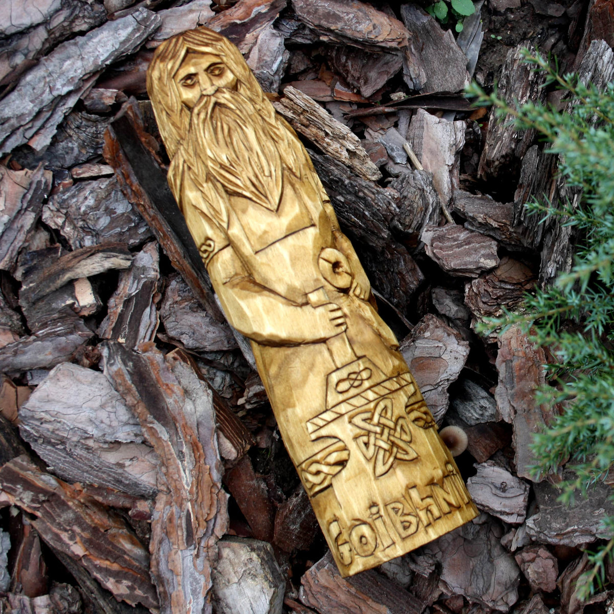 Hand-carved Goibhniu Celtic god statue displayed on bark, showing its elongated shape
