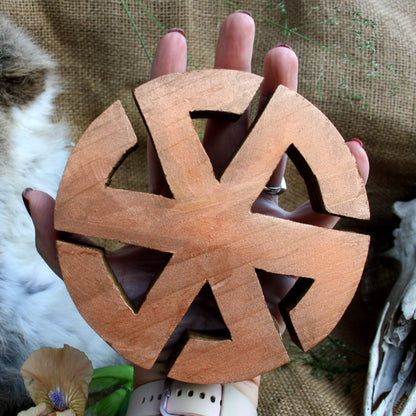 Hand holding wooden Kolovrat symbol showing its 14 cm size