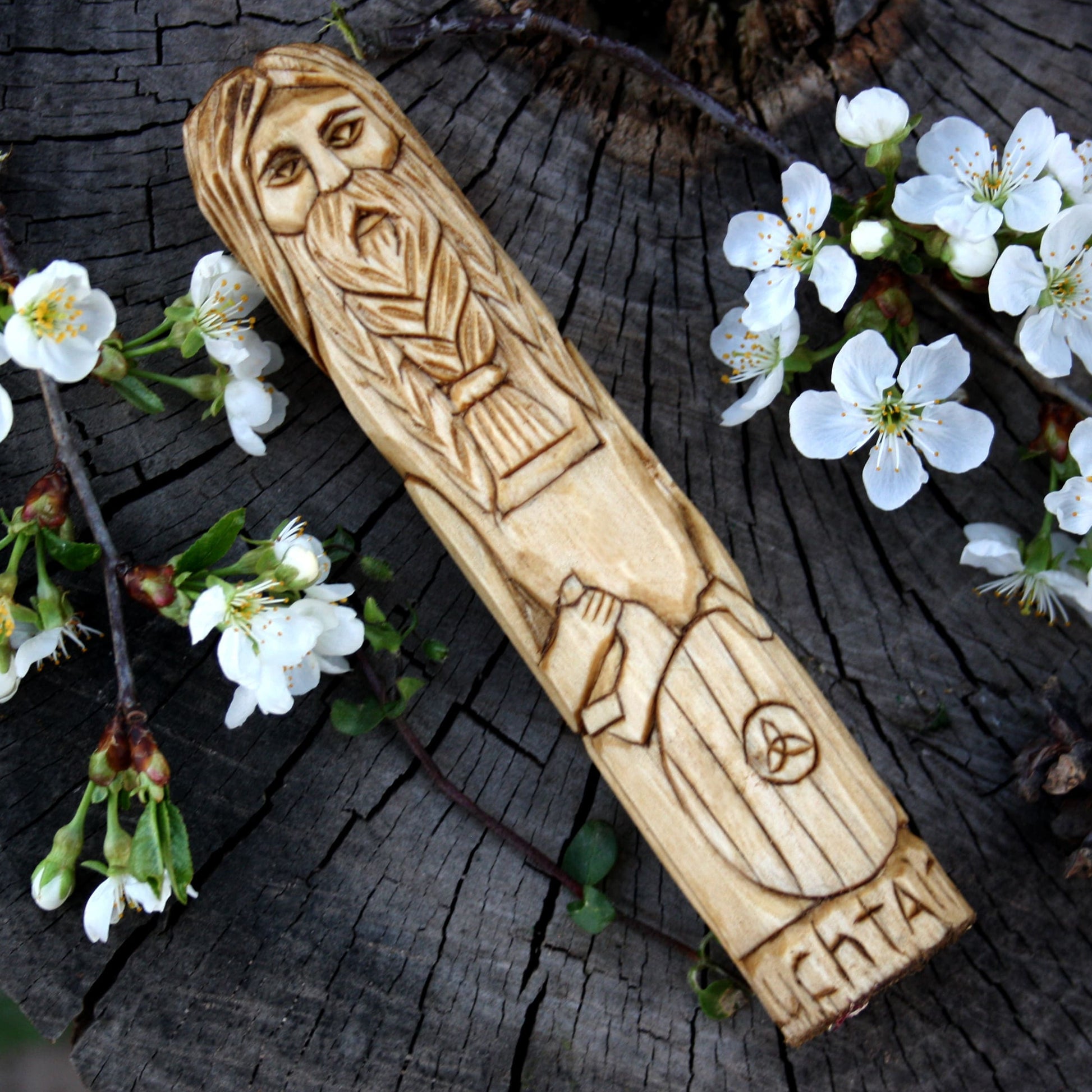Luchtaine Celtic god 15cm wooden statue placed diagonally on a weathered tree stump surrounded by small white blossoms.