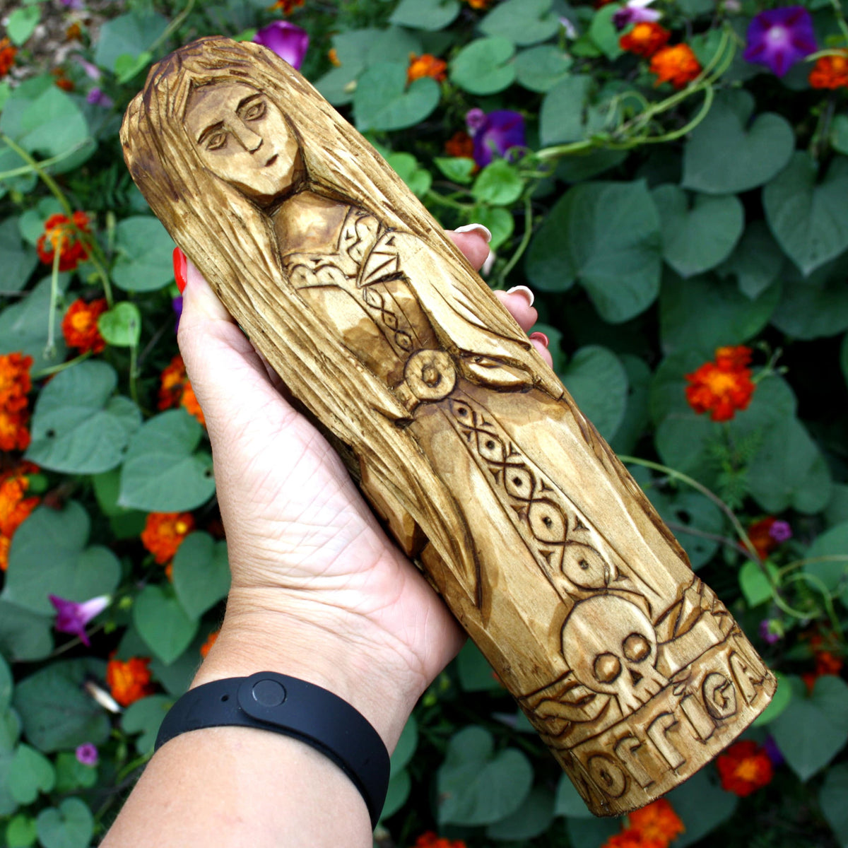 Hand holding the 25 cm wooden Morrigan sculpture to show its size and carved details