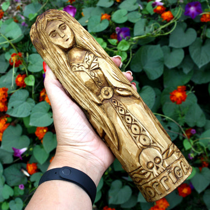 Hand holding the 25 cm wooden Morrigan sculpture to show its size and carved details