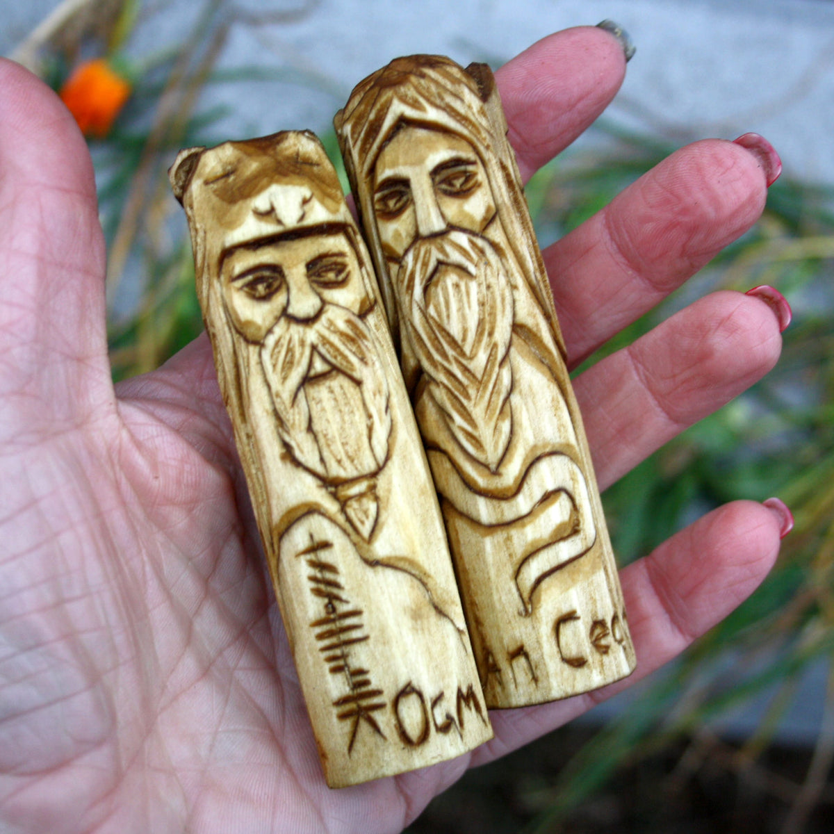 Two 10 cm Celtic wooden figurines held in a hand to demonstrate their compact size